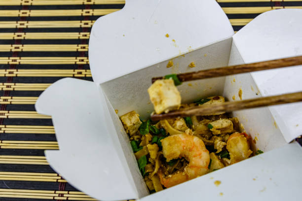Paper box with pad thai on bamboo mat. Chopsticks with tofu