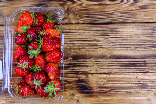 istock Plastic container with pile of ripe strawberries on wooden table. Top view 1369890130