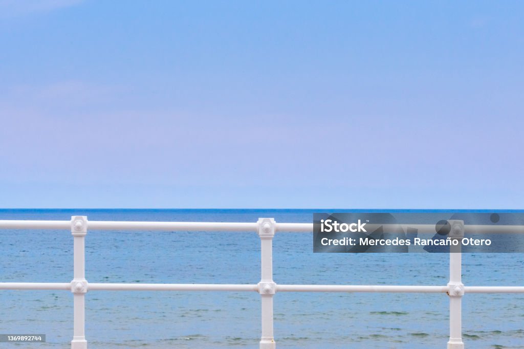 Seascape from San Lorenzo beach, waterfront promenade in Gijón, Spain. Seascape from San Lorenzo beach, waterfront promenade in Gijón, Asturias, Spain . White cast iron railing in the foreground. Clear sky and horizon over water in the background. Beach Stock Photo