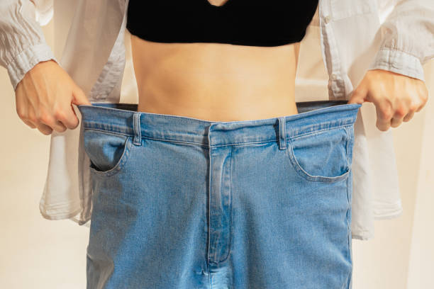 Slim figure of woman in wide jeans Cropped shot of young slim woman standing with naked belly in wide jeans and black top showing successful weight loss diet and wellness concept kilogram stock pictures, royalty-free photos & images