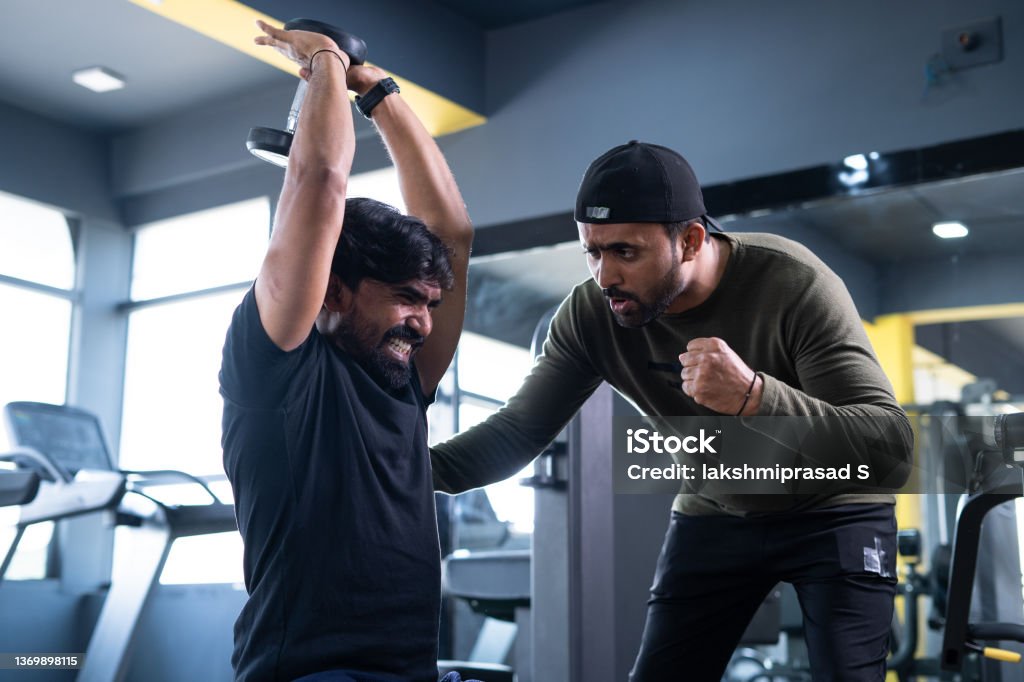 focus on client, Trainer motivating athlete to push his limits during workout at gym - concept of intense exercise, bodybuilding, determination and personal trainer focus on client, Trainer motivating athlete to push his limits during workout at gym - concept of intense exercise, bodybuilding, determination and personal trainer. Gym Stock Photo