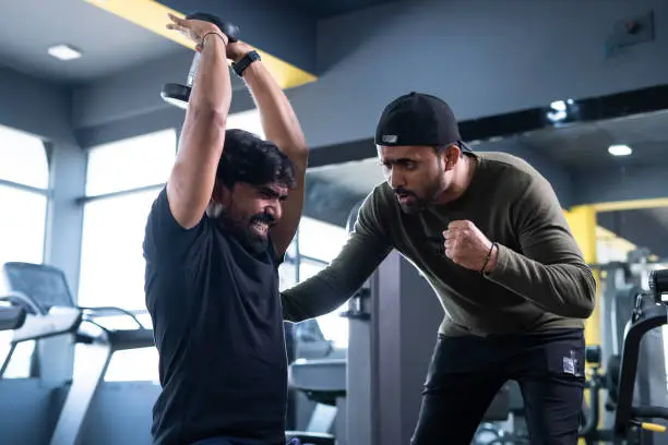 Photo of focus on client, Trainer motivating athlete to push his limits during workout at gym - concept of intense exercise, bodybuilding, determination and personal trainer