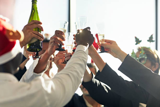 Celebratory toast with champagne at office Christmas party Close-up of multiethnic group of corporate executives raising their glasses to toast their success at year-end. office party stock pictures, royalty-free photos & images
