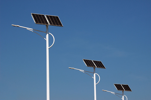 Row of three street lamp posts with solar powered energy panels against a clear blue sky background.
