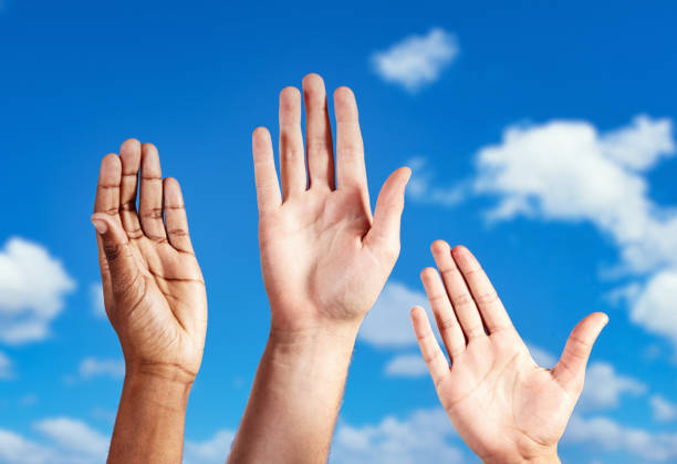 istock Three diverse open hands, palms visible, being held aloft, waving against a blue summer sky with puffy clouds 1369901931