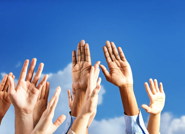 istock Many hands raised to heaven, praying or worshiping, against a blue sky with some puffy clouds 1369902499