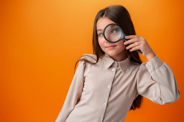 little girl child looking through a magnifying glass on orange background. - searching child curiosity discovery imagens e fotografias de stock