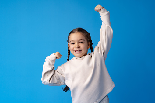 Little cute girl showing her strength on blue background, close up