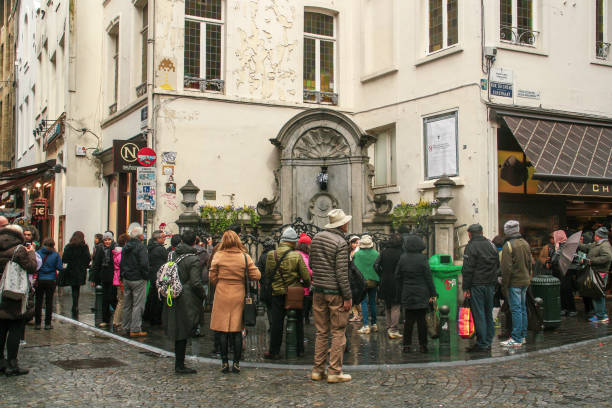 Tourists visiting the famous Statue Manneken Pis in Brussels. Brussels, Belgium; 04 29 2016. Statue dressed in traditional costume and tourists taking pictures of it. manneken pis statue in brussels belgium stock pictures, royalty-free photos & images