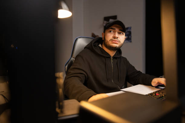 istock A thoughtful man in cap and sweatshirt sits in front of computer, an infromathematician works remotely from home at night, thinking about solving a technical problem, creating software 1369904623