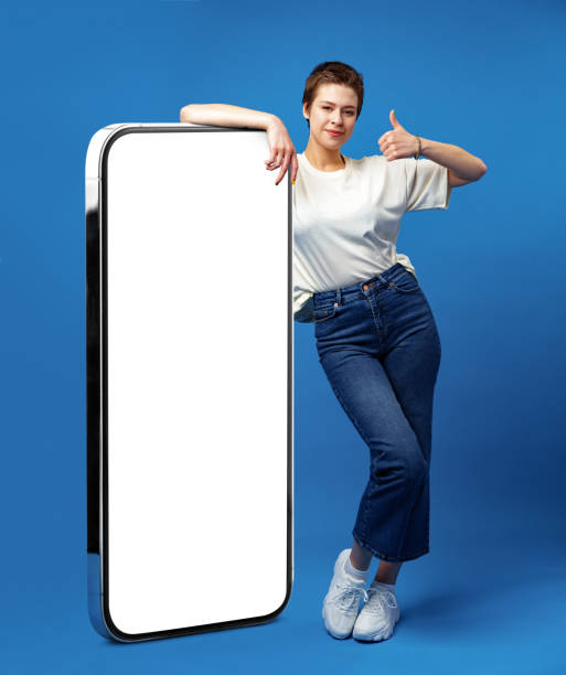 istock Happy young woman leaning on huge cellphone with empty white screen, for your ad, mock up 1369905565