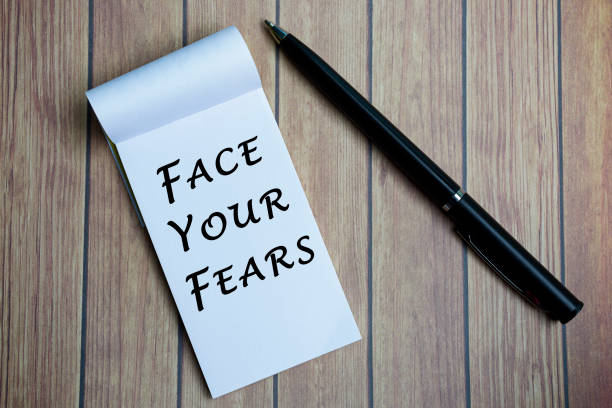 istock Face your fears text on notepad with a pen on a wooden desk. 1369905616