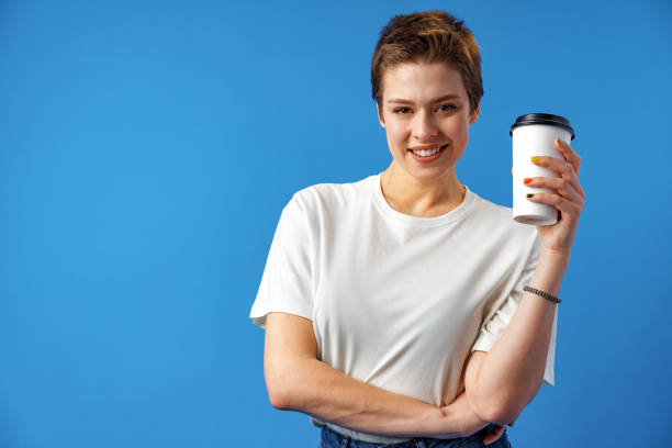 istock Beautiful smiling woman drinking coffee against blue background 1369906122