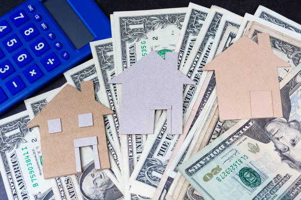 istock Brown paper house model with dollar banknotes and blue calculator 1369907319