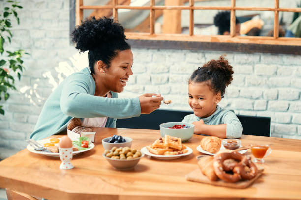 istock Happy black mother feeding her small daughter during breakfast at dining table. 1369908212
