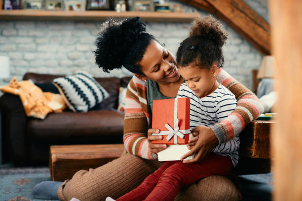 счастливые чернокожие мама и дочь вместе открывают подарочную коробку дома. - подарок стоковые фото и изображения