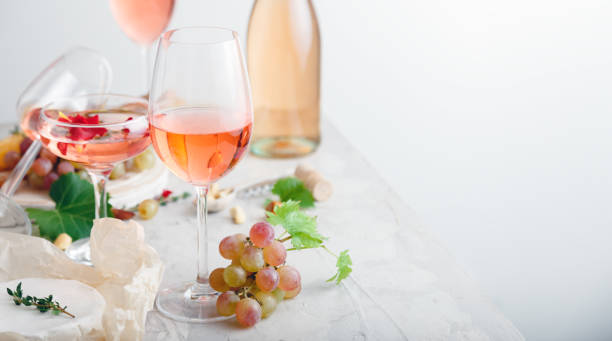 istock Rose wine in different wineglasses bottle on white table with grapes cheese, snacks bouquet of flowers. modern still life Rose Wine composition on light grey concrete background. Web banner copy space 1369911614