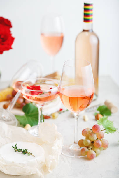 istock Rose wine in different wineglasses bottle on white table with grapes cheese, snacks bouquet of flowers. modern still life Rose Wine composition on light grey concrete background. Vertical photo 1369911619