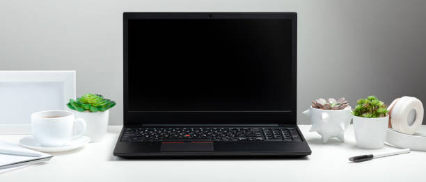 istock Black laptop with blank display layout template on white background. Office desk workspace in Home interior. White table with laptop for remote work or study. Long web banner with copy space 1369912946