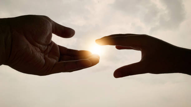 istock Hands reaching out to each other with bright shining sunlight. 1369913997