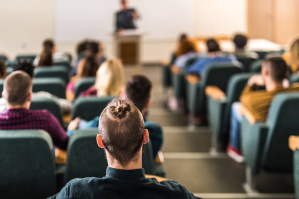 istock Rear view of large group of students on a class at lecture hall. 1369916992