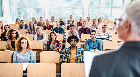 Un gran grupo de estudiantes universitarios escuchando a su profesor en una clase. photo