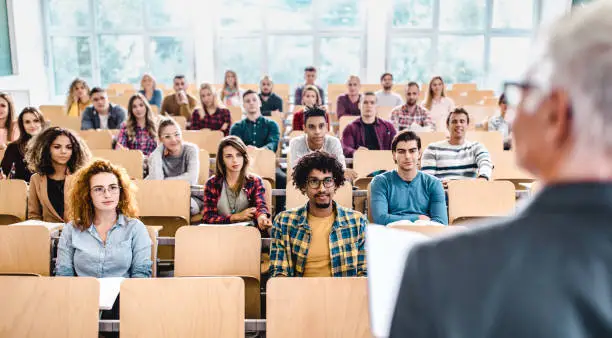 Panoramic view of large group of college students paying attention during a class in amphitheater.