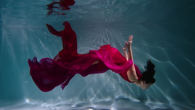 Magical underwater shot of a young woman swimming underwater. Red dress