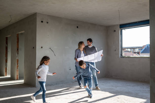 Happy family analyzing plans at their new apartment Young happy family examining blueprints during home building process in the apartment. Boy and girl are playing around. rebuilding stock pictures, royalty-free photos & images