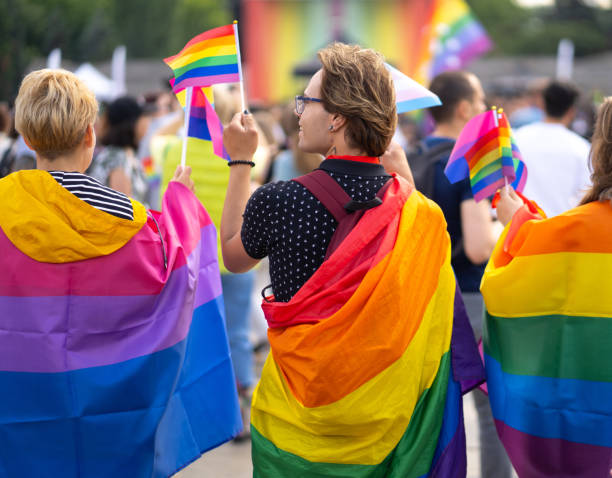 Watching a pride parade Gay and transgender and bisexual people protesting and supporting at pride event outdoors, wearing and holding rainbow flags on a sunny day transgender protest stock pictures, royalty-free photos & images