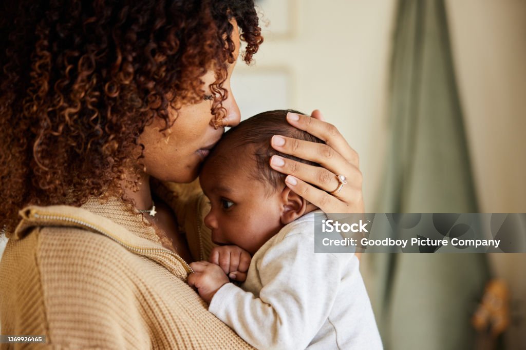Mother kissing with her baby boy in her arms Close-up of a loving mother kissing her adorable little baby boy cradled in her arms at home Mother Stock Photo