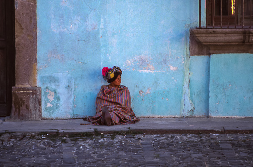 Antigua, Guatemala - aug 16, 1988: a woman of Indian ethnicity rests sitting on the ground leaning against a blue wall in the streets of Antigua