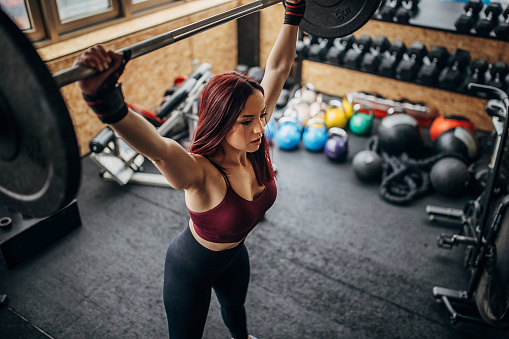 One woman, beautiful fit young woman exercising with weights in gym alone.