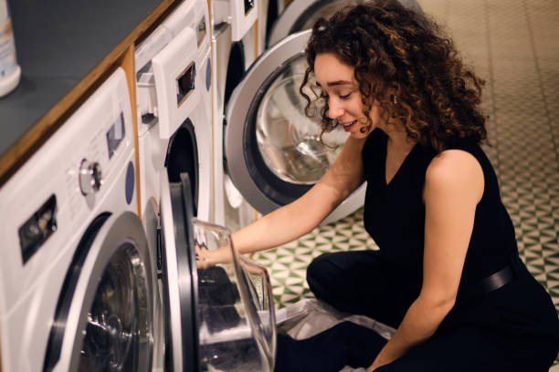 istock Beautiful dreamy girl loading clothes into washing machine in self-service laundry 1369932394