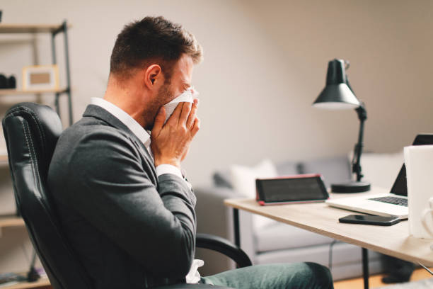istock Young man has a cold at work and wipes his nose with a tissue 1369932792