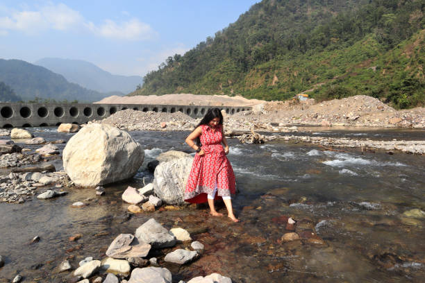 Young woman of Indian ethnicity standing in Ganges river and enjoying cold water during summer season in Shivpuri, Rishikesh, Uttarakhand, India.