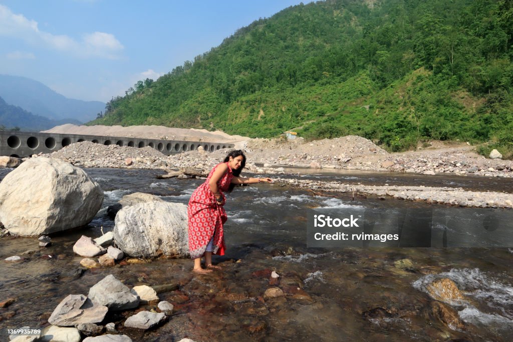 Young female of Indian ethnicity standing in Ganges river, Rishikesh, India Young woman of Indian ethnicity standing in Ganges river and enjoying cold water during summer season in Shivpuri, Rishikesh, Uttarakhand, India. Dress Stock Photo