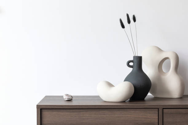 istock Minimalisitic composition of modern living room interior with brown commode, vase and sculptures. White wall. Copy space. Template. 1369936197