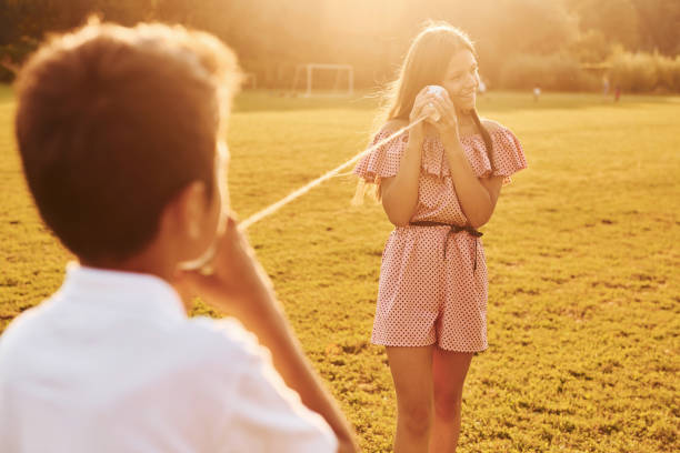 istock Boy with girl having fun by using tin can telephone while standing outdoors on the field 1369936236