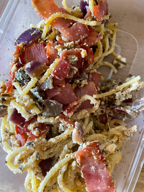 Full frame image of plastic, disposable takeaway container of homemade spaghetti carbonara recipe, pasta dish featuring beaten egg, bacon and parmesan cheese, fork, elevated view Stock photo showing elevated view of a plastic, disposable takeaway container of homemade spaghetti carbonara recipe. Pasta dish of spaghetti, bacon lardons, egg and Parmesan cheese, being eaten for dinner. cooked selective focus vertical pasta stock pictures, royalty-free photos & images