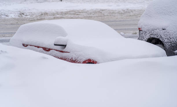 Parked vehicles covered with snow in winter blizzard in parking lot. Stuck cars under snow and ice. Buried vehicle in snowdrift on road. stock photo