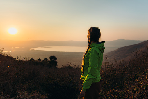 Young woman in green jacket meets beautiful sunrise above volcanic crater in Ngorongoro National Park, East Africa