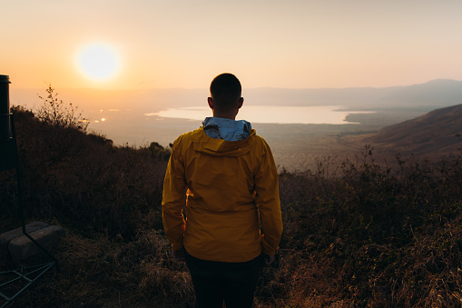 Young man in yellow jacket meets beautiful sunrise above volcanic crater in Ngorongoro National Park, East Africa