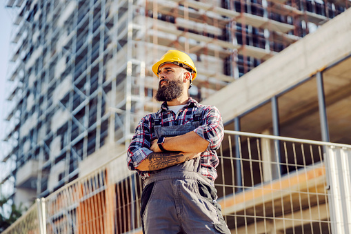 A serious handyman with arms crossed standing at construction site.