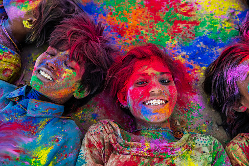 Group of happy Gypsy Indian children playing happy holi on sand dunes in desert village, Thar Desert, Rajasthan, India. Children are lying in a circle. Color powders are on their faces and clothes. Holi is a religious festival in India, celebrated, with the color powders, during the spring.