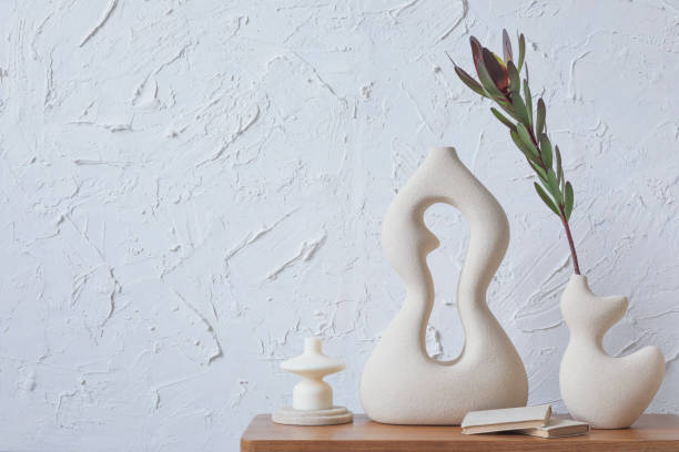Creative composition of minimalist home interior with handmade clay vases, sidetable and elegant personal accessories. Copy space. Wallpaper. Template.