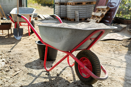 Construction wheelbarrow with cement and a shovel on the background of a stack of gray  tiles.