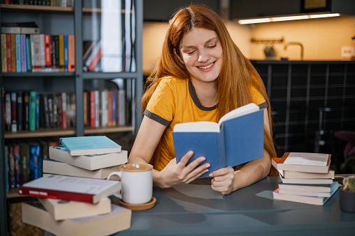 Young redhead woman sitting at the desk and reading a book