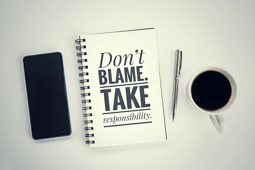Inspirational motivational positive quote on a notebook - Don't blame, take responsibility. With spiral book, pen, phone and cup of coffee on white table. Business responsible and commitment concept.