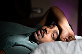 young man unable to sleep during night at bedroom - concept of suffering from insomnia, thoughtful and problems